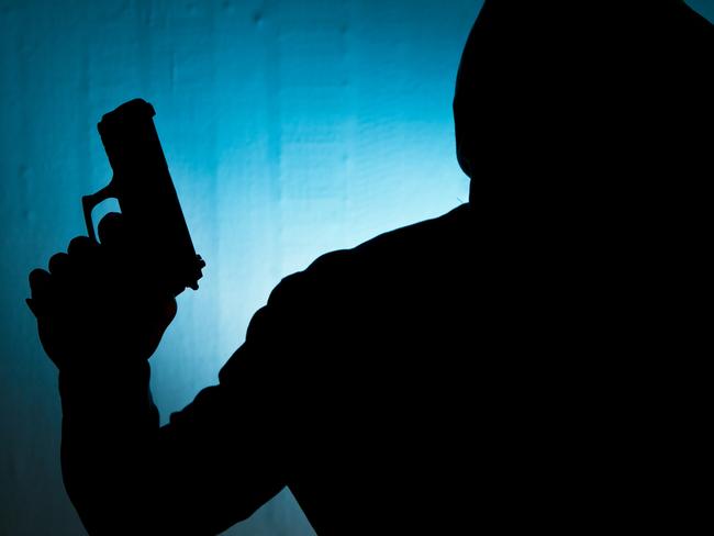 Silhouetted man with gun against blue wall background