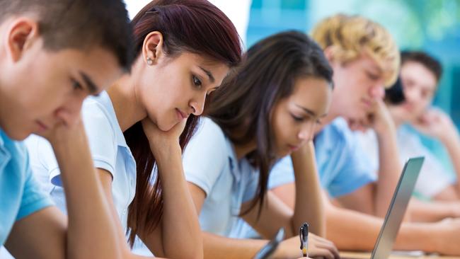 Row of private high school students work on assignment in class. They are writing or using laptops or digital tablets. They are concentrating as they study. They are wearing school uniforms.