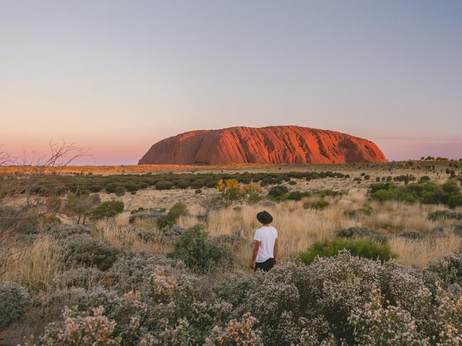 ESCAPE: A visitor stands in the desert landscape looking at Uluru during sunset.One of the great natural wonders of the world, Uluru towers above the surrounding landscape. Uluru is not only a spectacular natural formation, but its a deeply spiritual place. You can feel a powerful presence the moment you first set eyes on it. Picture: Tourism NT/Jason Van Miert