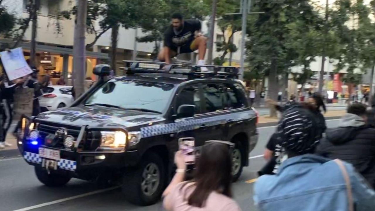 Topai-Aveai climbs on top of the cop car as friends and fellow protesters encourage him to get down.