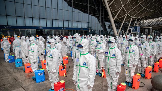 TOPSHOT - Staff members line up at attention as they prepare to spray disinfectant at Wuhan Railway Station in Wuhan in China's central Hubei province on March 24, 2020. - China announced on March 24 that a lockdown would be lifted on more than 50 million people in central Hubei province where the COVID-19 coronavirus first emerged late last year. (Photo by STR / AFP) / China OUT