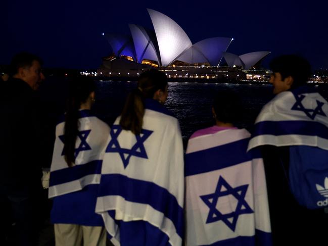 People with Israeli flags watch the Opera House while it is illuminated in blue to show solidarity with Israel in Sydney. Picture: AFP