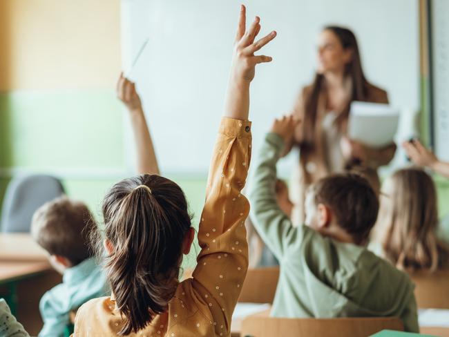 Students raising hands while teacher asking them questions in classroom