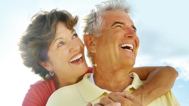 Portrait of a cheerful woman embracing a senior man from behind against sky