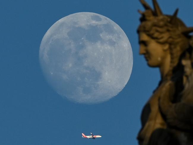 TOPSHOT - A plane flies by a statue of the Louvre as the waxing gibbous moon rises in Paris, on May 3, 2023. (Photo by Stefano RELLANDINI / AFP)