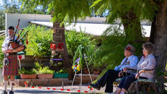 Sydney and June Kinsman watch as Neil Ross plays bagpipes in their driveway on Anzac Day 2020. Picture: Emma Murray