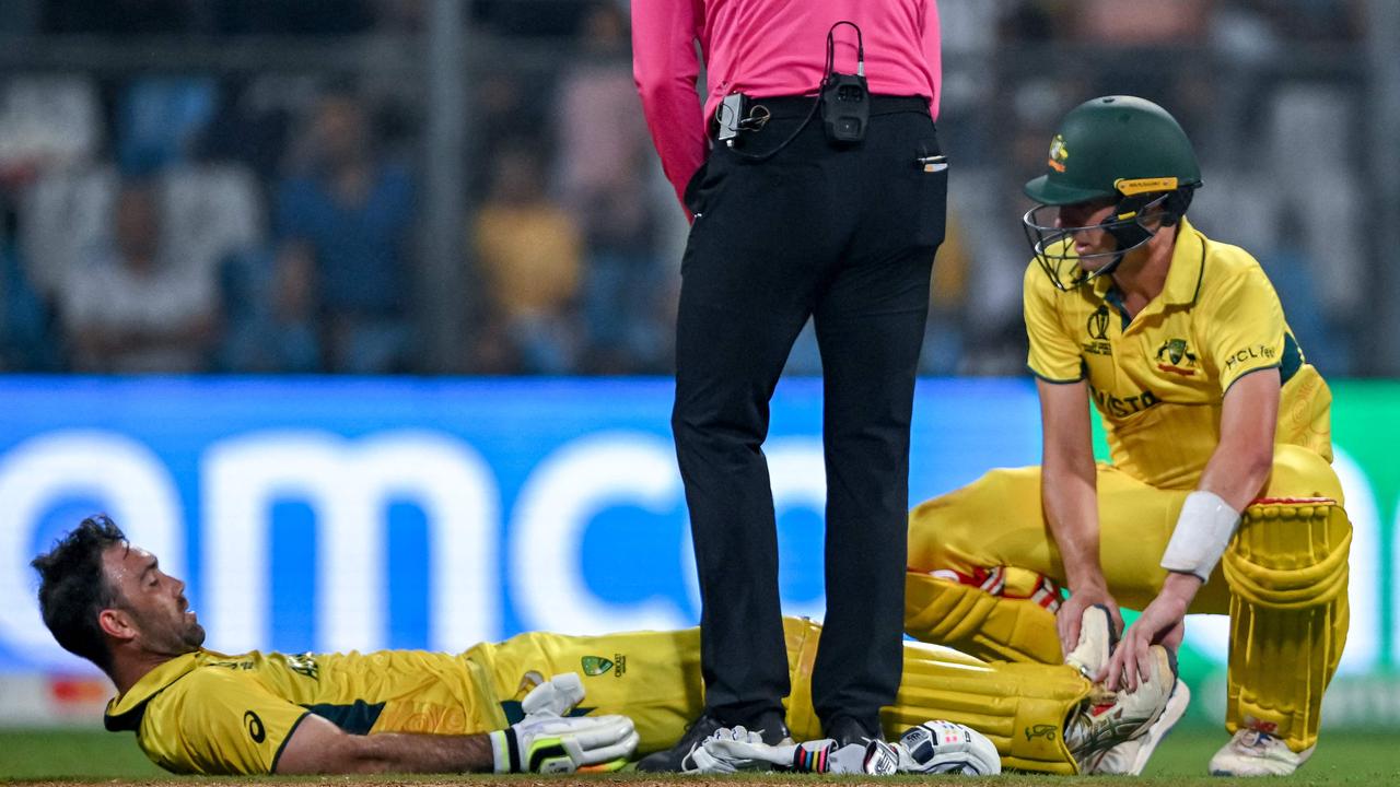 Maxwell (bottom) is helped by Pat Cummins after cramping. (Photo by INDRANIL MUKHERJEE / AFP)