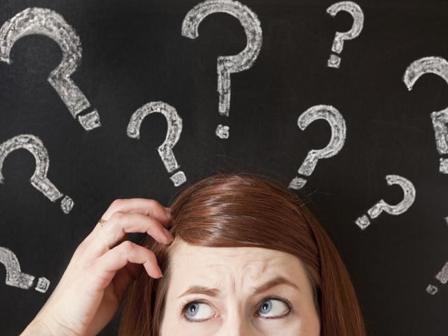 A confused scratching her head woman standing in front of a chalkboard with question marks written all over it.