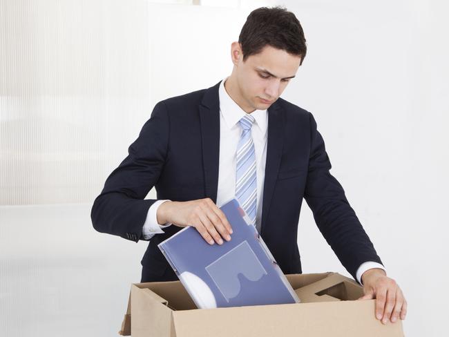 Sad young businessman packing files in cardboard box at desk in office