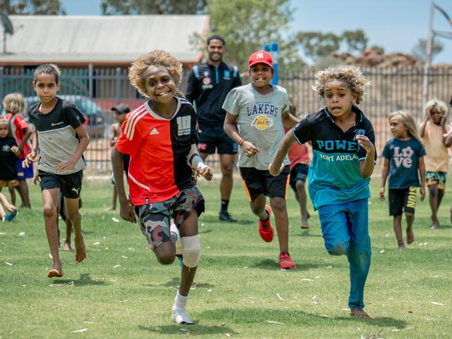 Students from Ernabella (Pukatja) Anangu School chase a football during a scratch match with Port Adelaide Football Club staff and players.