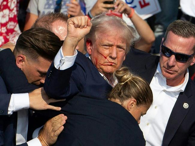 TOPSHOT - Republican candidate Donald Trump is seen with blood on his face surrounded by secret service agents as he is taken off the stage at a campaign event at Butler Farm Show Inc. in Butler, Pennsylvania, July 13, 2024. Donald Trump was hit in the ear in an apparent assassination attempt by a gunman at a campaign rally on Saturday, in a chaotic and shocking incident that will fuel fears of instability ahead of the 2024 US presidential election. The 78-year-old former president was rushed off stage with blood smeared across his face after the shooting in Butler, Pennsylvania, while the gunman and a bystander were killed and two spectators critically injured. (Photo by Rebecca DROKE / AFP)