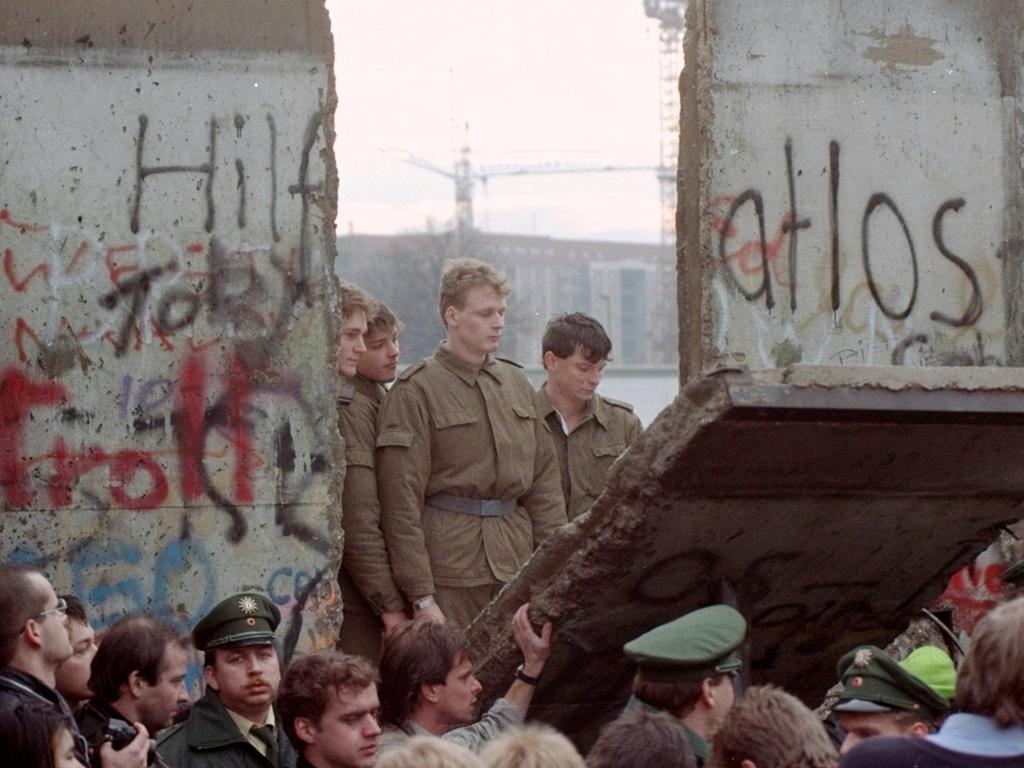 East German border guards are seen through a gap in the Berlin Wall after demonstrators tear down a section on November 11. Picture: AP Photo/Lionel Cironneau, File