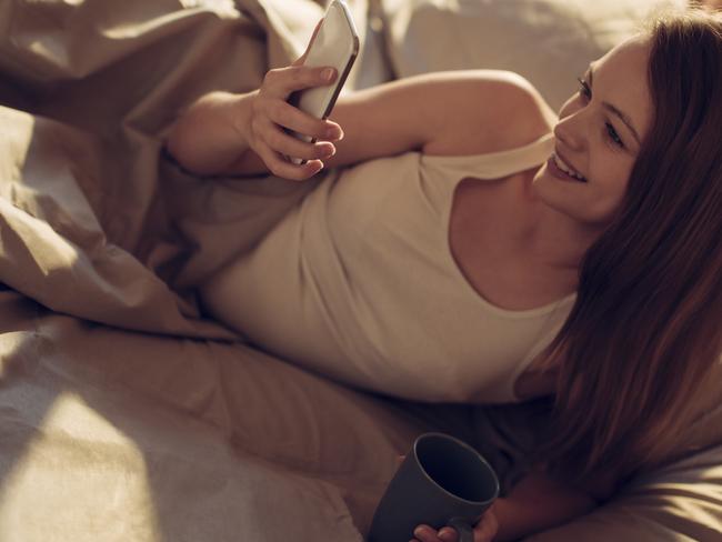 Close up of a young woman using smart phone while lying in bed