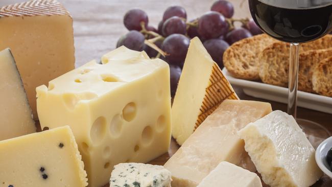 Assorted cheeses (such as ementhal, blue cheese, pecorino, parmesan and manchego among others) served with bread, grapes, black olives and a glass of red wine on a wooden table. Typical appetizer from mediterranean culture. Studio photography. High angle view. Natural day lighting. Still life. Horizontal composition.