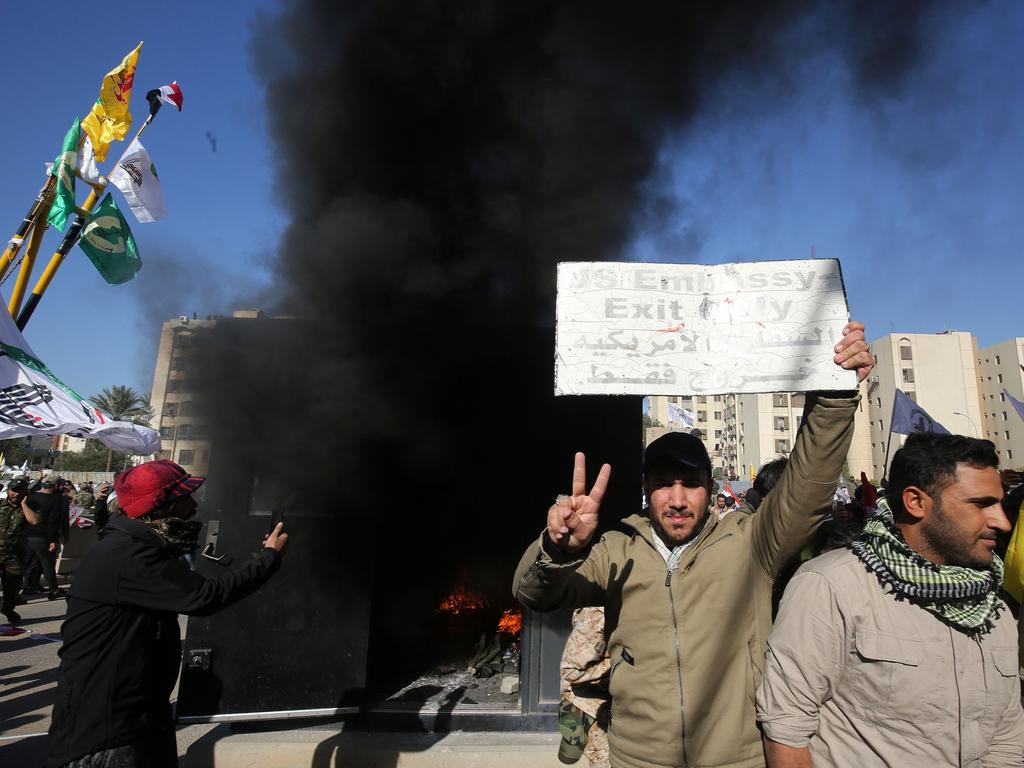 An Iraqi protester holds up a sign that was detached from the US embassy wall as a sentry box is set ablaze in front of the building in the capital Baghdad. Picture: AFP