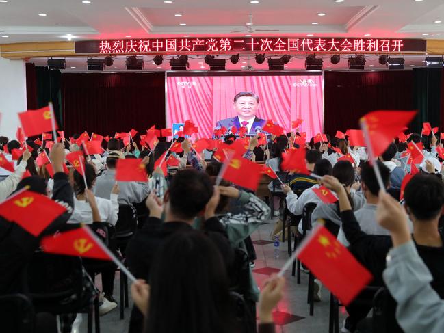 TOPSHOT - This photo taken on October 16, 2022 shows people waving national flags and Communist Party flags as they watch the opening session of the 20th Chinese Communist Party Congress in Huaibei, in Chinaâs eastern Anhui province. - President Xi Jinping hailed China's rise as a global power and demanded unity around his leadership on October 16, launching a Communist Party Congress that is set to rubber stamp his bid to rule for a historic third term. (Photo by AFP) / China OUT