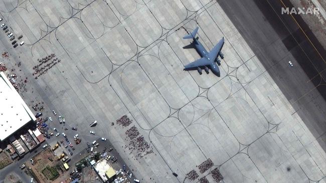 Crowds of people wait on the tarmac, awaiting evacuation.