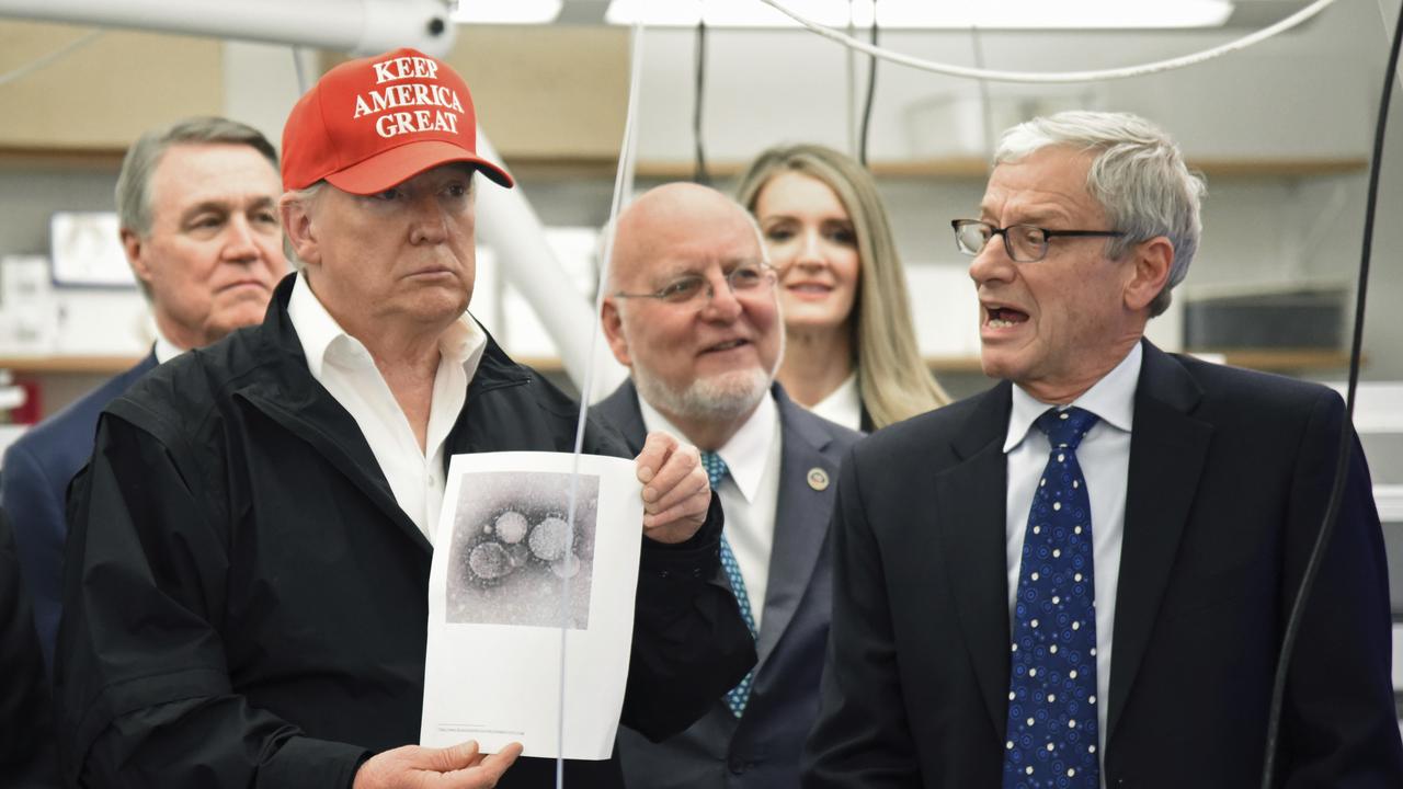 President Donald Trump holds a photograph of coronavirus as Dr Steve Monroe, right, from the CDC speaks to members of the press at the headquarters of the Centers for Disease Control and Prevention in Atlanta on Friday. Picture: Hyosub Shin/Atlanta Journal-Constitution via AP