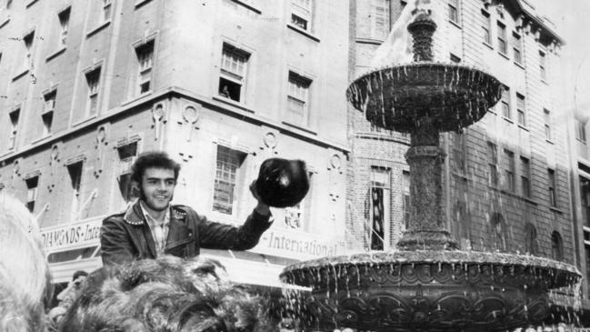 A motorcycle rider holds his helmet high after dipping it into the champagne-filled fountain at the opening of Rundle Mall on September 1, 1976.