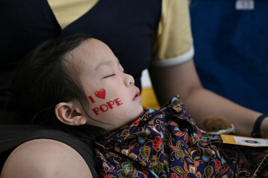 A child falls asleep as Catholic faithful wait to attend the holy mass led by Pope Francis at the National Stadium in Singapore on September 12, 2024.