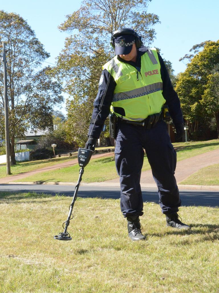 A forensic police officer sweeps a grassy area on the New England Highway looking for spent bullet casings that may be linked to the murder of 25-year-old Toowoomba man Thor Morgan.