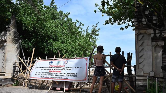 Foreign tourists look on at the beach from behind a barrier with a closure notice in Kuta near Denpasar. Picture: AFP