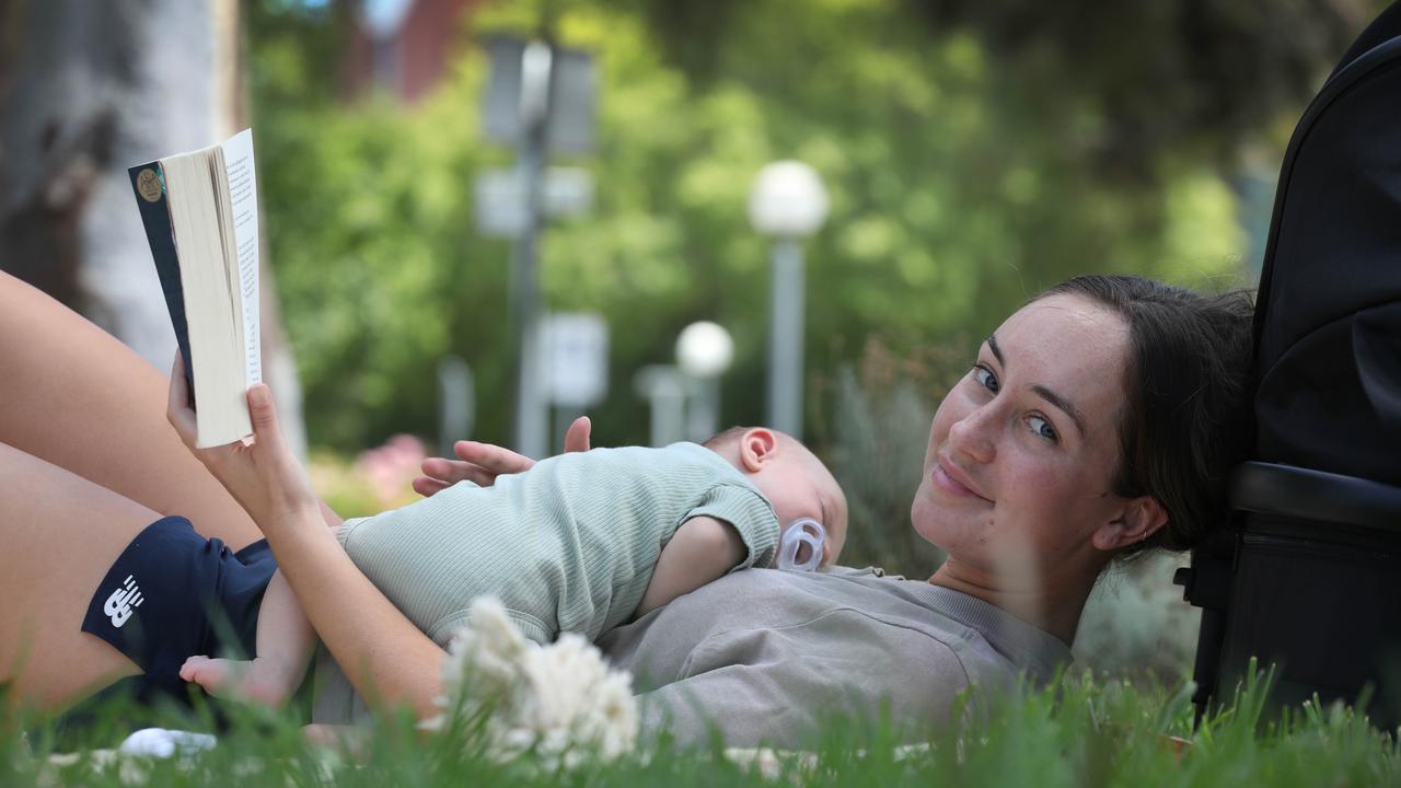 Jasmine Wilson of St Claire found a cool spot in Victoria Park to read her book, with seven-week-old Harley Schneider. Picture: NCA NewsWire/ Dean Martin