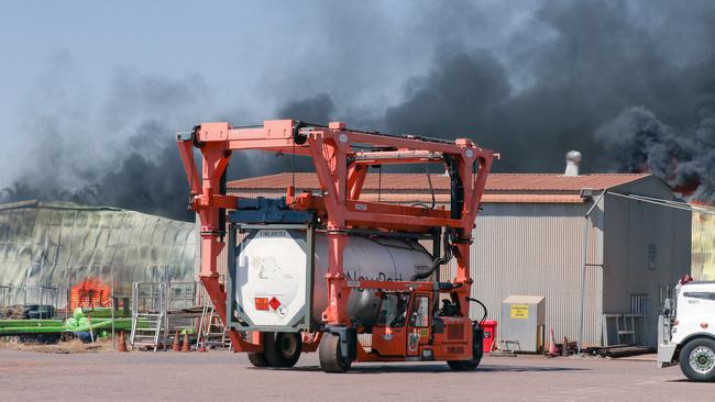 Workers move containers of aviation fuel from the path of a massive blaze on College Rd near a fuel storage depot in Berrimah. Picture: Glenn Campbell