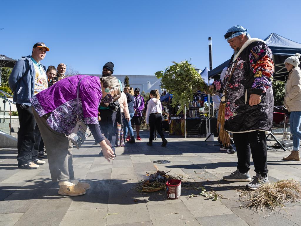 Barbara Walker lets the smoke waft over her as Jarowair Wakka Wakka man Conrad Bauwens conducts a Smoking Ceremony at the NAIDOC arts and craft market at Grand Central, Saturday, July 9, 2022. Picture: Kevin Farmer