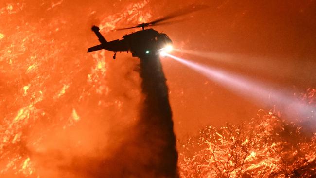 A fire fighting helicopter drops water as the Palisades fire grows near the Mandeville Canyon neighborhood and Encino, California. Picture: AFP