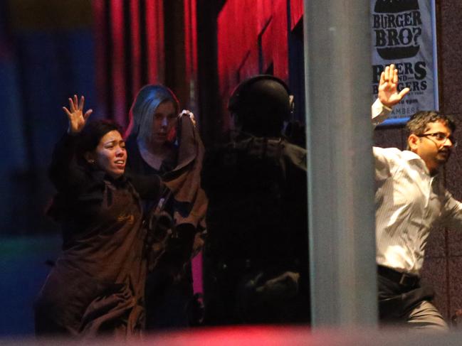 FILE - In this Dec. 16, 2014 file photo, hostages run towards armed tactical response police for safety right after the police stormed into a cafe under siege at Martin Place in the central business district of Sydney, Australia. Two staff members of the Lindt Cafe said in paid interviews broadcast Sunday, Feb. 8, 2015 by Nine Network television that they had armed themselves with box cutters after gunman Man Horan Monis took them and 16 other people hostage in the cafe downtown Sydney. (AP Photo/Rob Griffith, File)