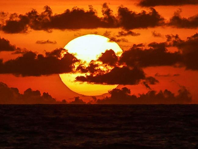 The sun sets behind the clouds on the horizon at a beach in the Kerobokan district on Indonesia's resort island of Bali on January 15, 2024. (Photo by David GANNON / AFP)