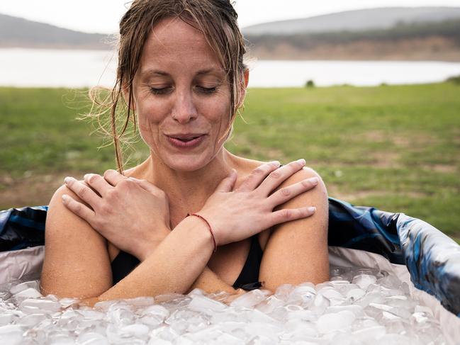 Woman inside a iced bath tube inhaling with eyes closed in the middle of a field