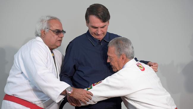 Brazilian far-right presidential candidate Jair Bolsonaro (C) receives an honorary black belt by Robson Gracie (L), son of the founder of the first Brazilian Jiu-Jitsu school, which was later turned into "Gracie Jiu-Jitsu", and Brazilian Jiu-Jitsu master Joa Carlos Austregesilo de Athayde (R) during a press conference in Rio de Janeiro, Brazil, on October 25, 2018. - The presidential runoff election takes place on October 28 in Brazil. (Photo by CARL DE SOUZA / AFP)