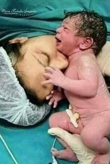 Woman laying on operating table with her child laying next to her head. 