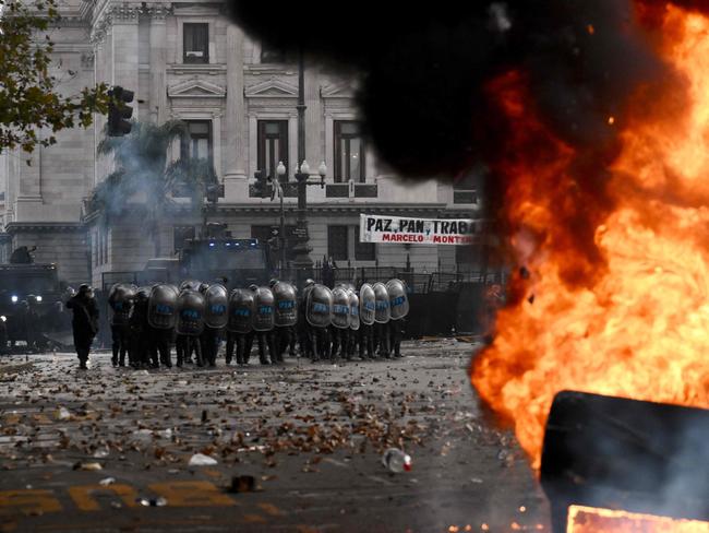 Anti-riot police officers stand guard behind a Cadena 3 radio station car on fire during a protest outside the National Congress in Buenos Aires on June 12, 2024. Argentine senators are discussing a key reform package for the ultra-right-wing president Javier Milei, in a session marked by strikes and demonstrations in front of Congress. (Photo by Luis ROBAYO / AFP)