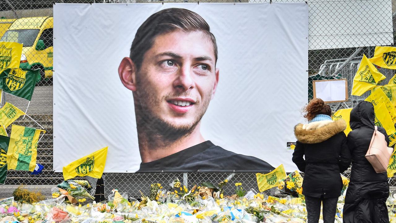 People look at yellow flowers displayed in front of the portrait of Argentinian forward Emiliano Sala.