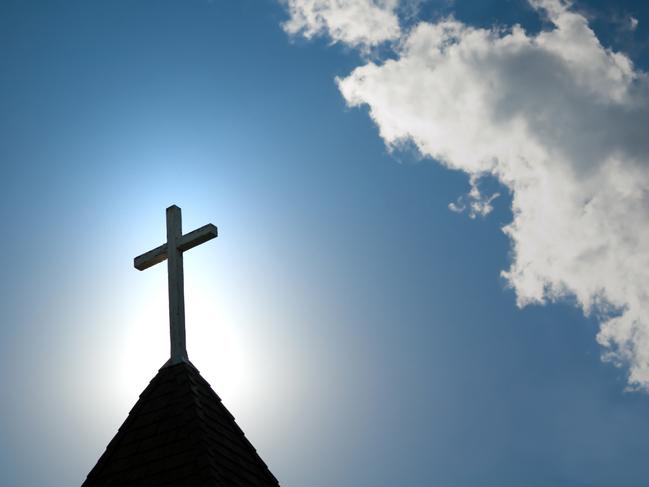 A wood cross on an old church steeple backlighted by a rising sun. Some copy space.