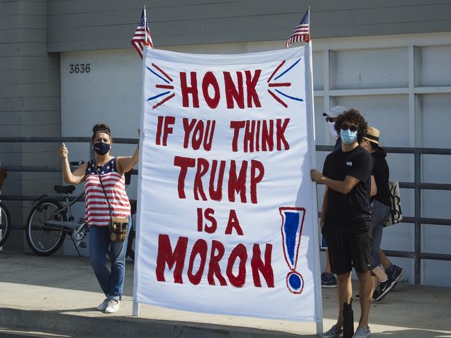 Summer Bailey (Left) holds a sign reading "Honk if you think Trump is a moron" along the route for President Donald Trump's motorcade in Newport Beach, California. Picture: Angus Mordant