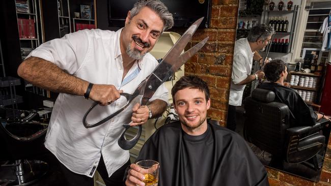 Former AFL player Dylan Buckley enjoys a snip and a sip while hairdresser Frank Ciccone gets to work. Picture: Jake Nowakowski