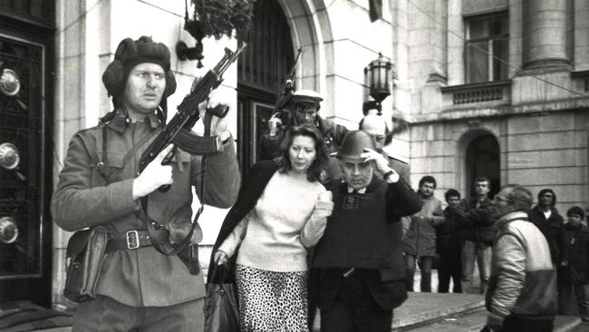 The woman suspected of having links with the dreaded Securitate is forced at gunpoint towards the heavy armoured vehicle to be taken away for questioning. Picture: Hedley Thomas