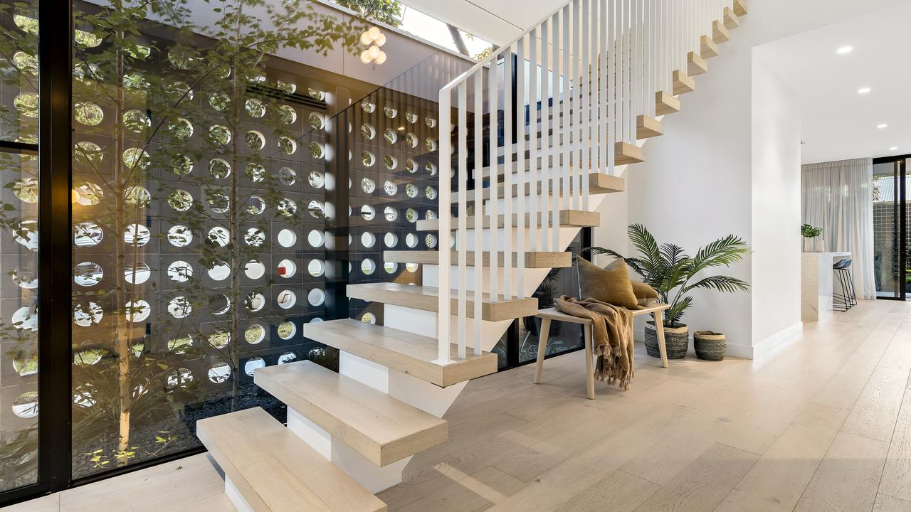 An indoor garden, walled on one side with glass and the other side with breeze blocks, sits next to a modern and minimalist-style staircase.