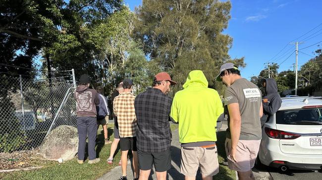 Workers are waiting to pick up their tools outside the gates of the Palmer Coolum Resort in Yaroomba.