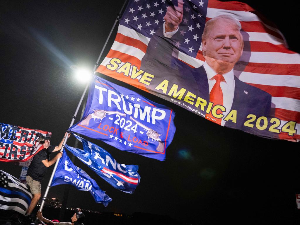 A supporter of US President-elect Donald Trump adjusts flags fluttering in wind as he and others await Trump’s motorcade near his home in Mar-a-Lago in Palm Beach, Florida on December 11. Picture: Roberto Schmidt/AFP