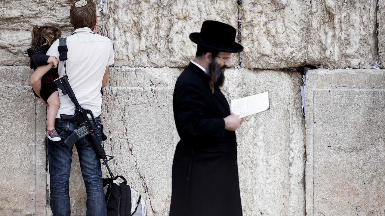 An armed Jewish man holds a child as he prays at the Western Wall, the last remaining vestige of the Second Temple, in Jerusalem's Old City. Picture: AFP