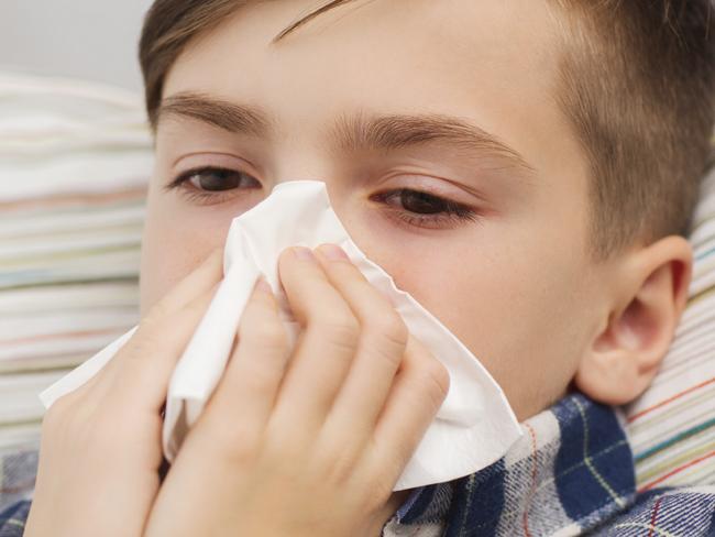 childhood, healthcare, rhinitis, people and medicine concept - ill boy with flu lying in bed and blowing his nose at home