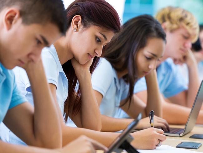 Row of private high school students work on assignment in class. They are writing or using laptops or digital tablets. They are concentrating as they study. They are wearing school uniforms.