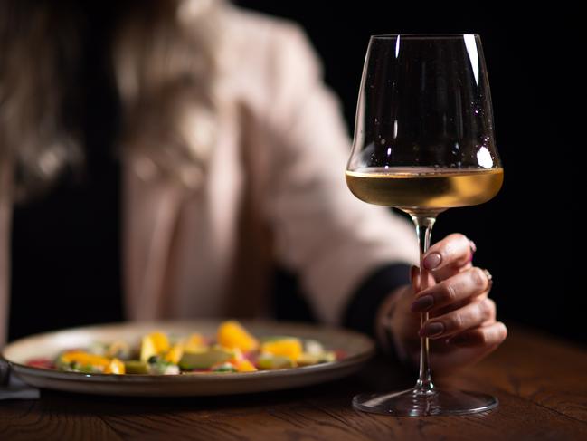 A woman holding a glass of white wine on a dark background in a restaurant. Photo: iStock