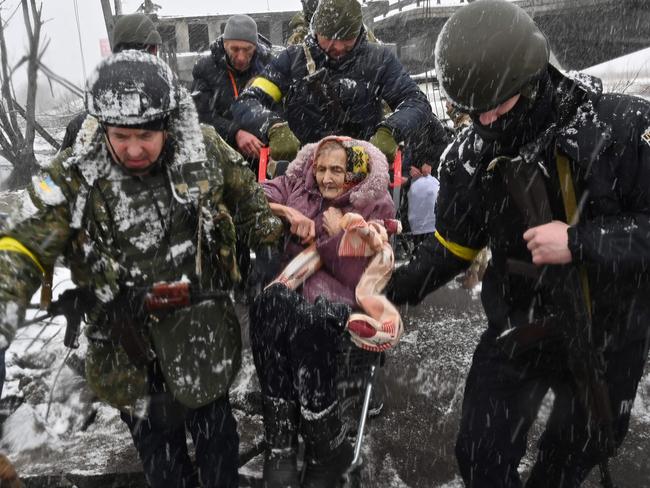 Ukrainian soldiers help an elderly woman to cross a destroyed bridge as she evacuates the city of Irpin, northwest of Kyiv. Picture: AFP