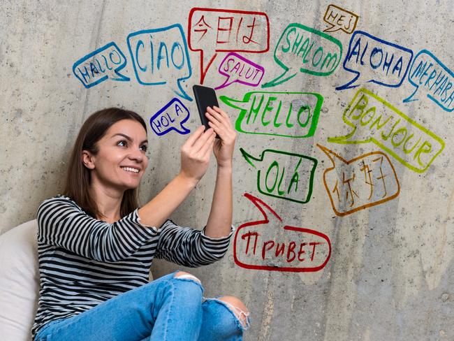 Happy woman chatting on smartphone . She is seating in front of a concrete wall with messages translated in many languages